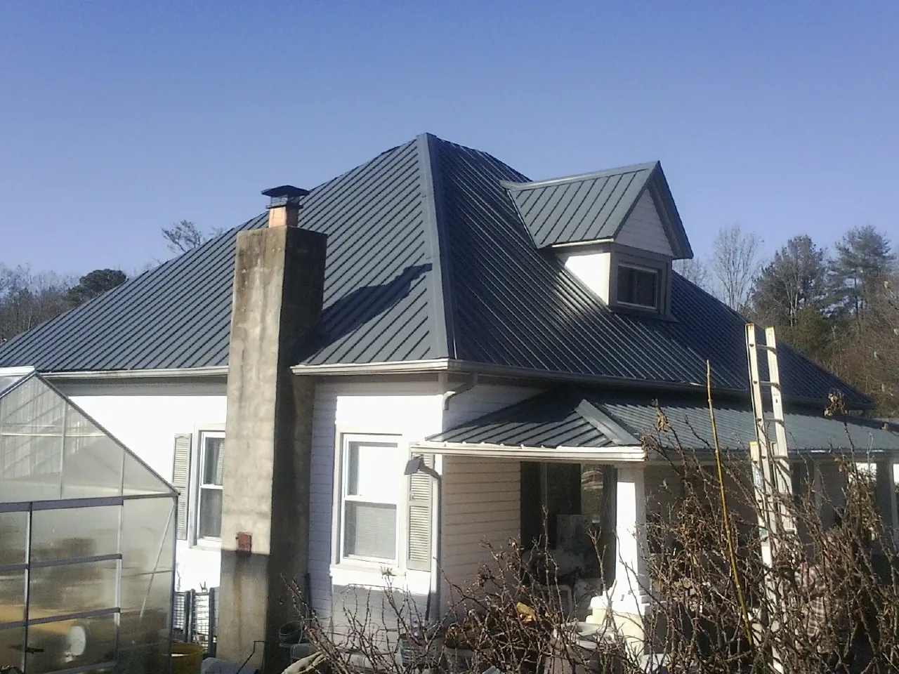 Dark blue standing seam metal roof on a white farmhouse with dormer — Slate & Tile Roof Repair by Roofing Brothers in North Babylon