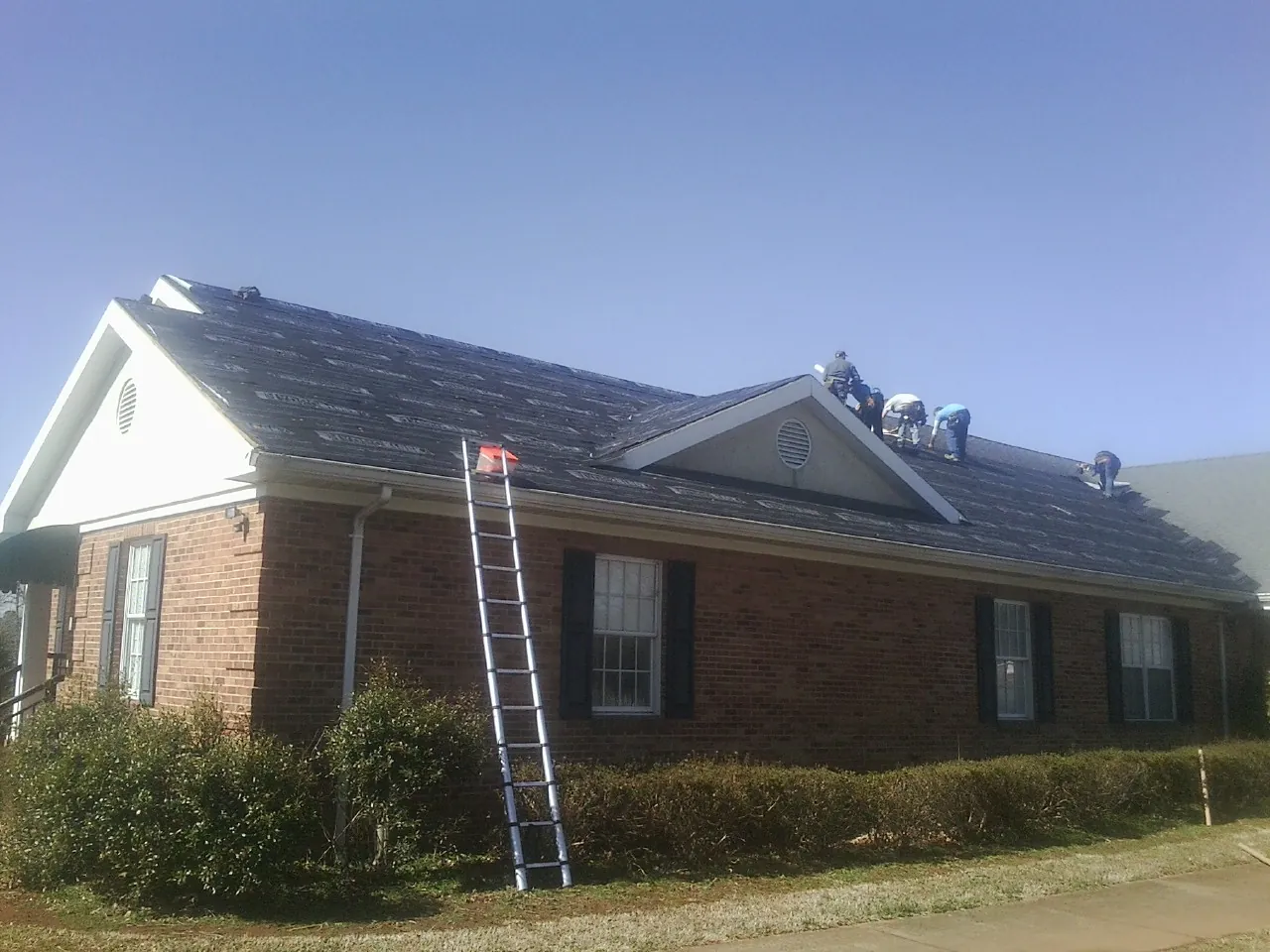 Crew tearing shingles off a brick ranch roof with a ladder set — Metal Roof Repair work by our crew in North Babylon