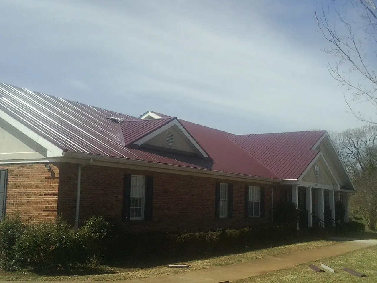 Red metal roof with gabled entries on a long brick building, from a Hail Damage Roof Repair job in North Babylon