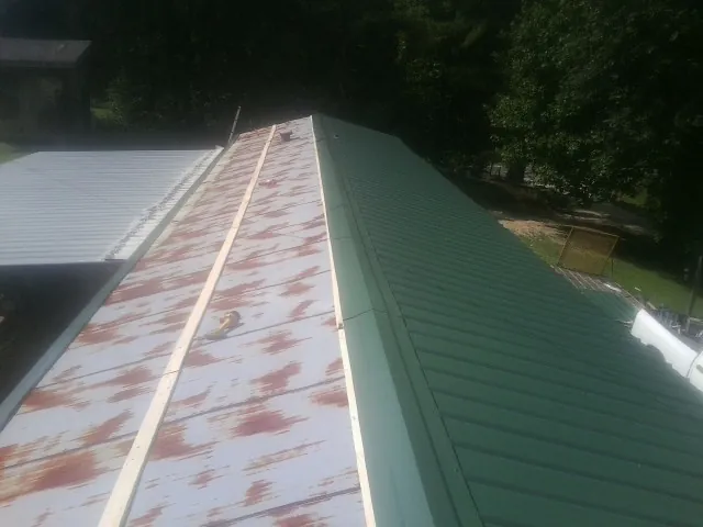 Old rusted panels beside newly installed green metal roofing — Wind Damage Roof Repair by Roofing Brothers in North Babylon