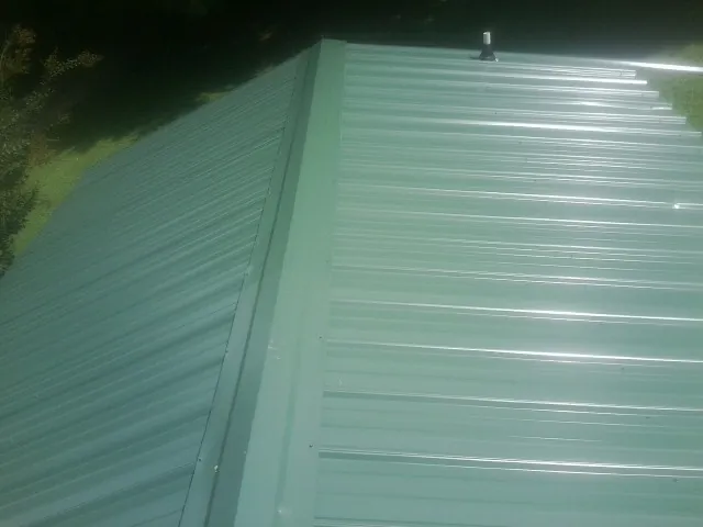 New green metal panels meeting at the ridge of a roof — Flat Roof Repair work by our crew in North Babylon