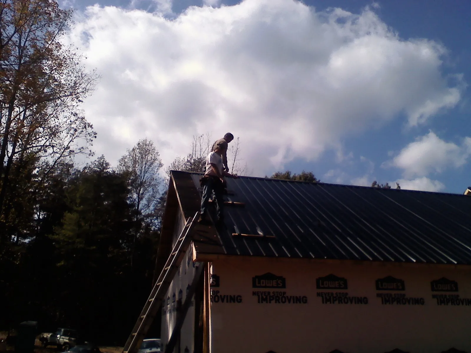 Roofer fastening dark metal panels high against a cloudy sky, from a Roof Inspection job in North Babylon