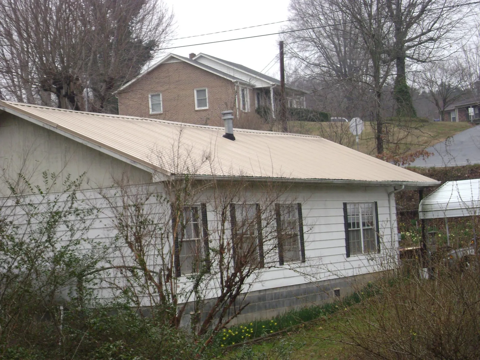 Tan metal roof on a white sided house set into a hillside — Commercial Roofing by Roofing Brothers in North Babylon